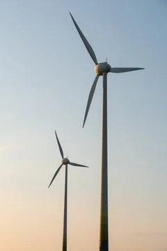 Two massive wind turbines stand tall against a clear pale sky during the go.. Stock Photos