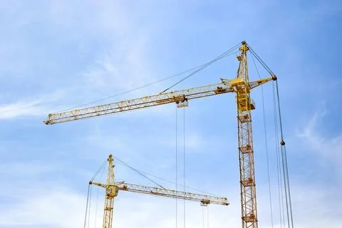 Two massive yellow tower cranes stand tall against a bright, slightly cloud.. Fotos de archivo