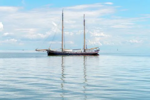 A two-masted ship is reflected on the surface of the water at sea Stock Photos