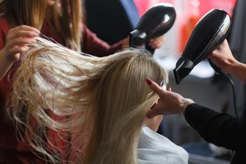 Two masters at the same time dried with hair dryers hair blonde model in beau Fotos de archivo