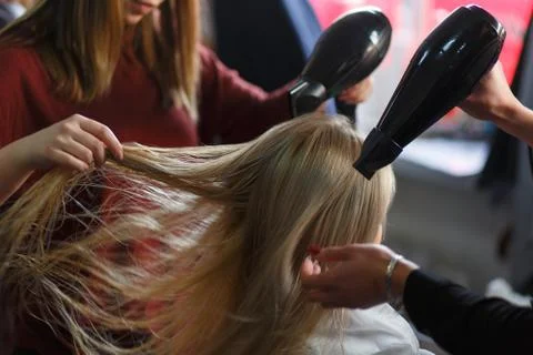 Two masters at the same time dried with hair dryers hair blonde model in beau Fotos Stock