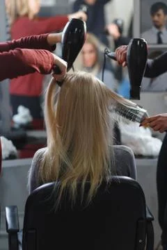 Two masters at the same time dried with hair dryers hair blonde model in beau Фото