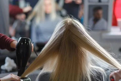 Two masters at the same time dried with hair dryers hair blonde model in beau Fotos Stock