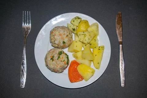 Two meat meatballs with boiled potatoes and boiled carrots on a white plate w Stock Photos