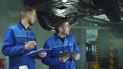 Two Mechanic checking on a car engine and taking notes Stock Footage 70644377