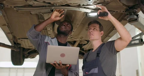 Two mechanic standing under broken car in large garage Stock Footage 259628166