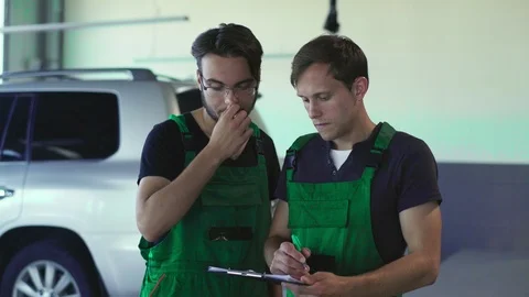 Two mechanics are looking at the scheme of the car. Both are young and dresse Stock Footage 94658129