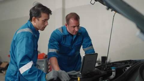 Two mechanics in blue uniforms examine a EV car engine Video stock 338332535