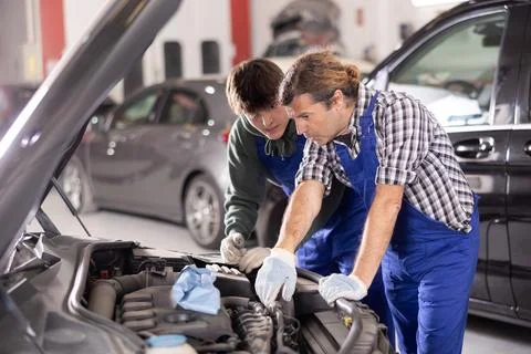 Two mechanics examining car engine under open hood in workshop Stock Photos
