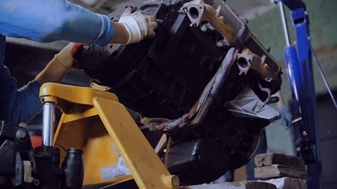 Two mechanics with the help of a crane load an automobile engine onto a cart Stock Footage 78832820