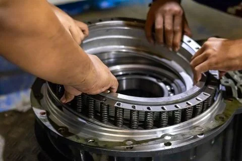 Two mechanics install a piston return spring assembly into a transmission. Foto stock