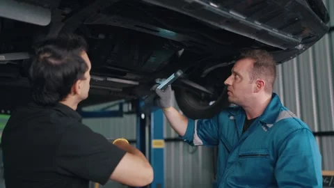 Two mechanics work beneath a raised EV car Stock-Footage 341461373