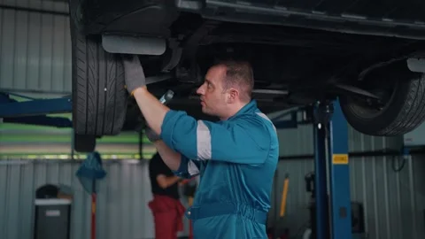 Two mechanics work beneath a raised EV car Stock-Footage 341461500