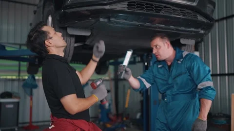 Two mechanics work under a lifted EV car Stock-Footage 341461371