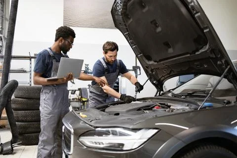 Two mechanics working on car engine with laptop in garage Stock Photos