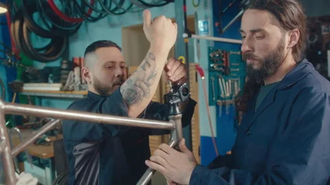 Two Mechanics Working Together on Bicycle Frame in Repair Shop Stock Footage 256596356