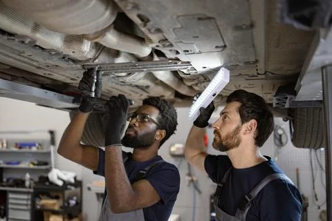 Two mechanics working under car in auto repair shop Stock Photos
