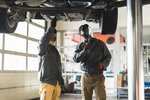 Two mechnics during work. One holding a flashlight, another inspecting car's Stock Photos