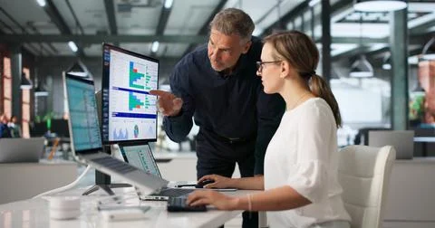 Two Medical Coders Analyze Spreadsheet Data On Laptops For Precise Billing Up Foto stock