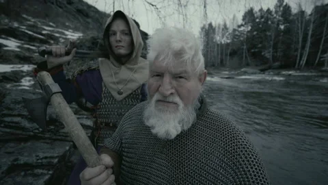​​Two Medieval Warriors Posing with Axe and Sword by River and Snowy Cliff Stock Footage 295532826