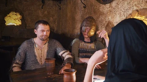Two medieval warriors sitting at table wit hooded figure, confident and confused Stock Footage 79463841