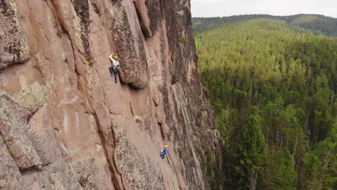 Two men are climbing a vertical granite wall in the middle of a forest. Stock Footage 131372177