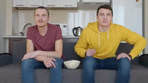 Two men are eating popcorn and watching a football match Stock Footage 107648936