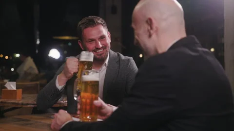 Two men are enjoying a friendly night out in a pub, raising their large glasses Stock Footage 289110596