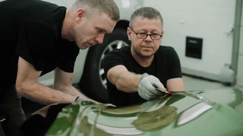 Two men are focused on the process of vinyl wrapping a car using plastic cards Stock Footage 171959533