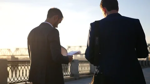 Two men are negotiating, walking down the street, holding documents in their Stock Footage 114601410