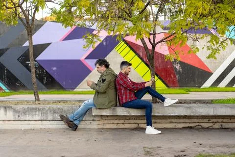 Two men are sitting back to back looking at their cellphones Stock Photos