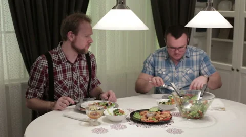 Two men are sitting at a table eating and talking Stock Footage 58653622