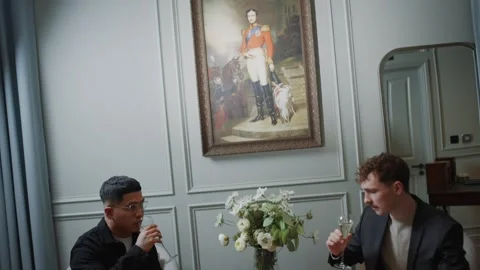 Two men are sitting at a table with a vase of flowers in front of them Video stock 295996693