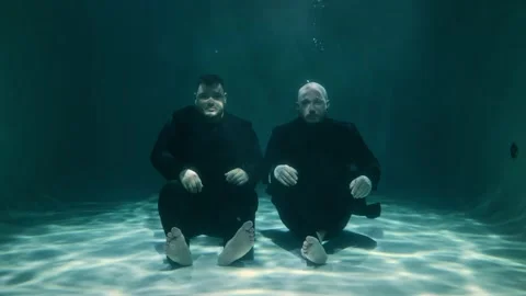 Two men are sitting underwater of the pool and looking at the camera Stock Footage 315559816