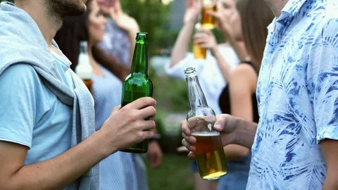 Two men are talking separately from the company, holding bottles of beer in Stock Footage 114271346