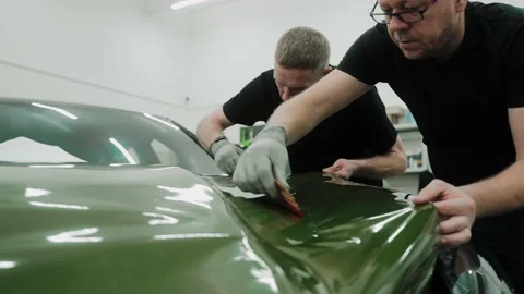 Two men are vinyl wrapping a car in dark green color using plastic cards Stock Footage 171958730