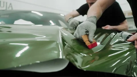 Two men are vinyl wrapping a car in khaki green color using plastic cards Stock-Footage 171959844
