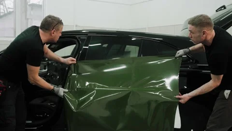Two men are vinyl wrapping a car in khaki green color, applying wrap to the door Video stock 171960077