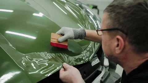 Two men are vinyl wrapping a car in dark green color using plastic cards Stock Footage 171960477