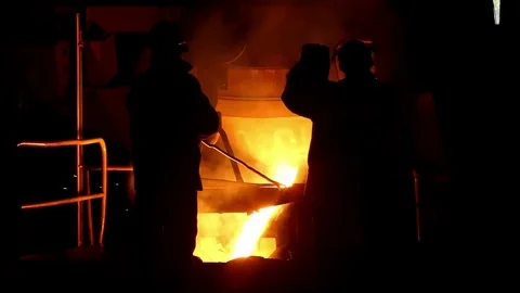 Two men are waiting until the drained hot liquid metal from the furnace Stock Footage 76856933