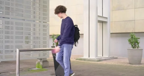 Two men arriving to wait at building, one pulling black suitcase, checking Stock Footage 341851654