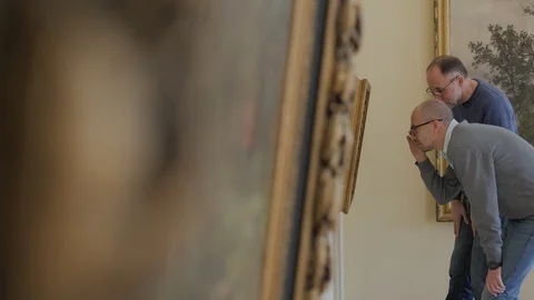 Two men in an art gallery look at a painting and talk about art Stock Footage 127984568