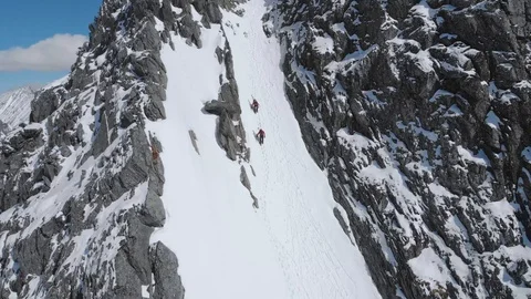 Two men ascending extreme mountain couloir with skis aerial view Stock Footage 99738330