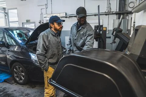 Two men auto mechanics mounting and balancing car wheel using diagnostic Stock Photos