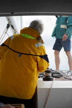 Two men, back of the captain with yellow rain jacket and first mate on sailboat Stock Photos