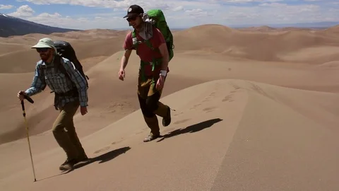 Two Men Backpacking Through Sand Dunes At Sand Dunes National Park Video stock 100694644