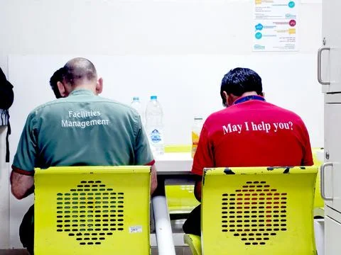 Two men, backs to the camera, sit at a table. One wears a green shirt labeled Foto stock