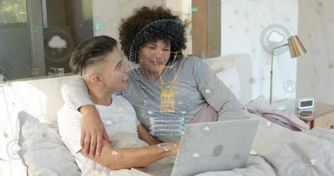 Two men on bed, left man tapping laptop touchpad, making cloud icons animate, Stock Footage 323354317