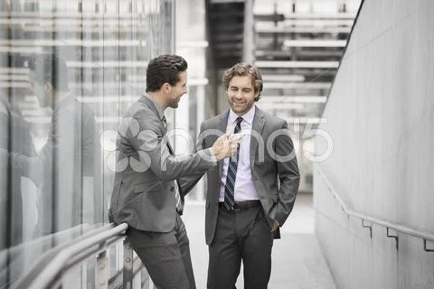 Two Men In Business Suits, One Holding A Smart Phone