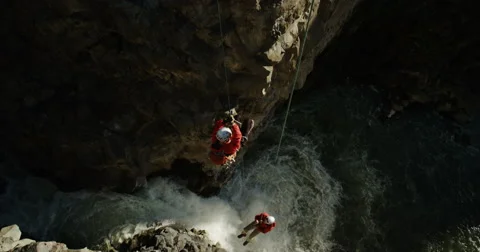 Two men canyoneering ascending up ropes over a beautiful waterfall slow motion Stock Footage 64343264